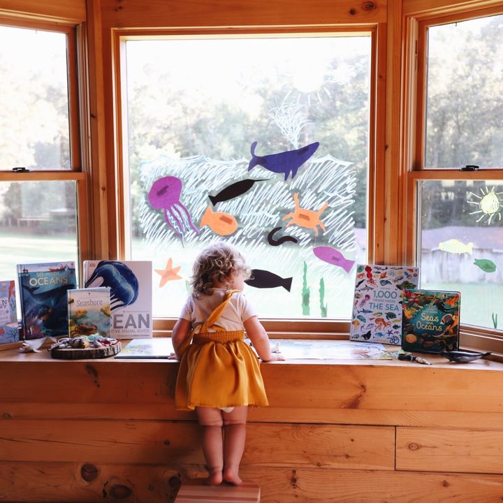 A little girl reading in a sunny window seat
